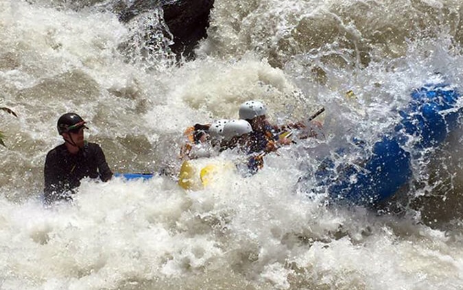 Action shot of a raft cresting a wave in the fast-moving Cheoah river, showcasing the excitement and adventure of rafting.
