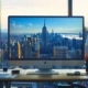 a modern, well-organized office workspace features a sleek computer screen displaying a vibrant and user-friendly online rafting booking interface, with a city skyline visible through a large window in the background.