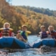 experience the thrill of family-friendly rafting in tennessee, where brightly colored inflatable rafts glide over sparkling blue waters, surrounded by a backdrop of rolling hills and vibrant autumn foliage. lively children, with exuberant smiles, eagerly hold paddles as they navigate through gentle rapids. the scene captures a sun-drenched riverbank with clear skies overhead, enhanced by the cheerful splashes of water reflecting the sunlight. each raft features distinct designs, showcasing the fun, adventurous spirit of family outings. this engaging moment is framed from a low angle, emphasizing the motion of the rafts and the excitement of the participants. shot with a sony a6100 using a sony e pz 18-105mm f4 g oss lens, the composition incorporates bright, vivid colors against a crisp, azure sky, with natural sunlight providing a warm glow, creating an inviting atmosphere for families.