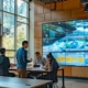 a dynamic office setting featuring a large digital display screen with flowing graph animations illustrating the ocoee river's flow rates, surrounded by focused professionals discussing rafting strategies.